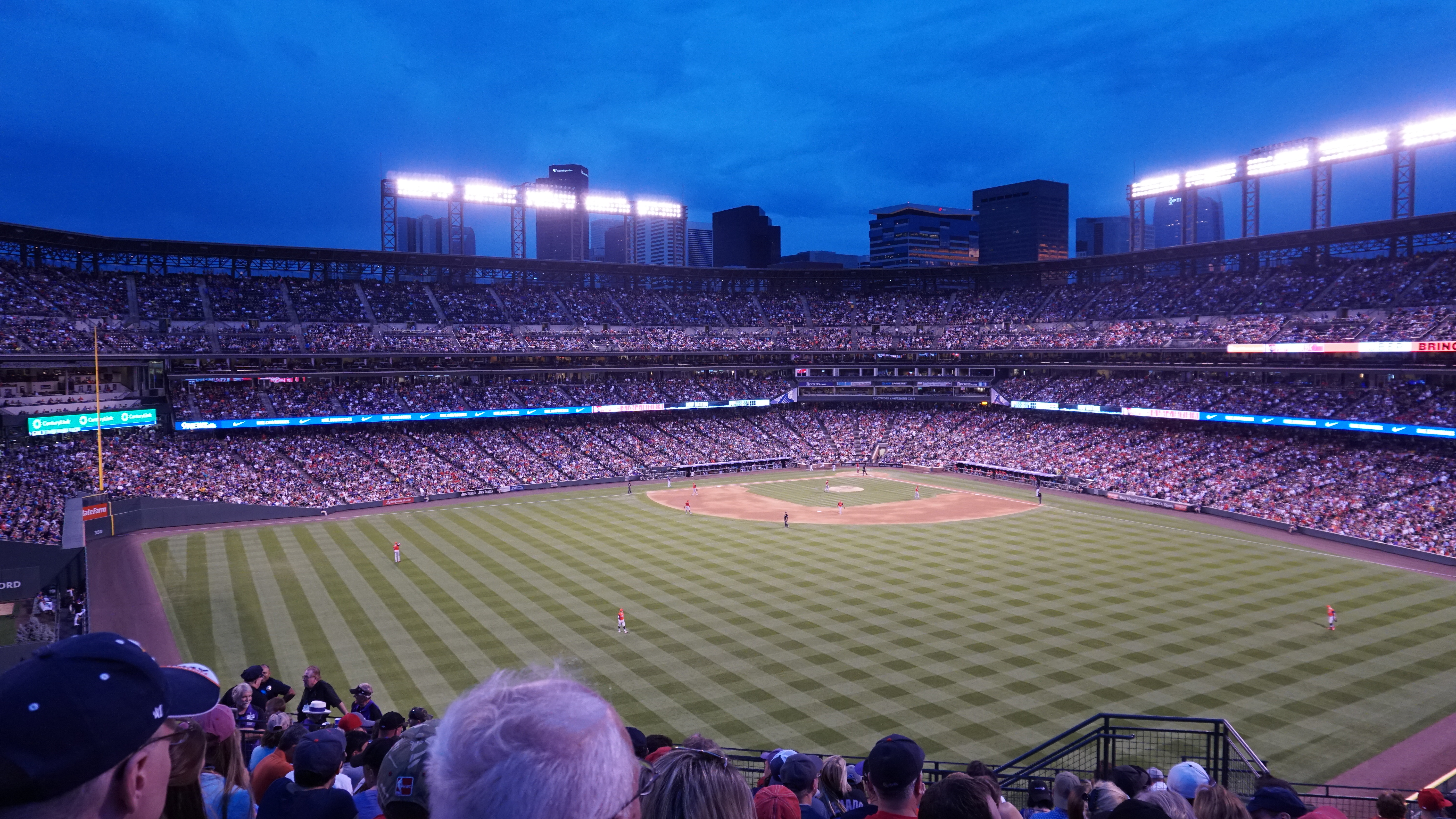 A baseball field and crowded stands beneath stadium lights at blue hour.