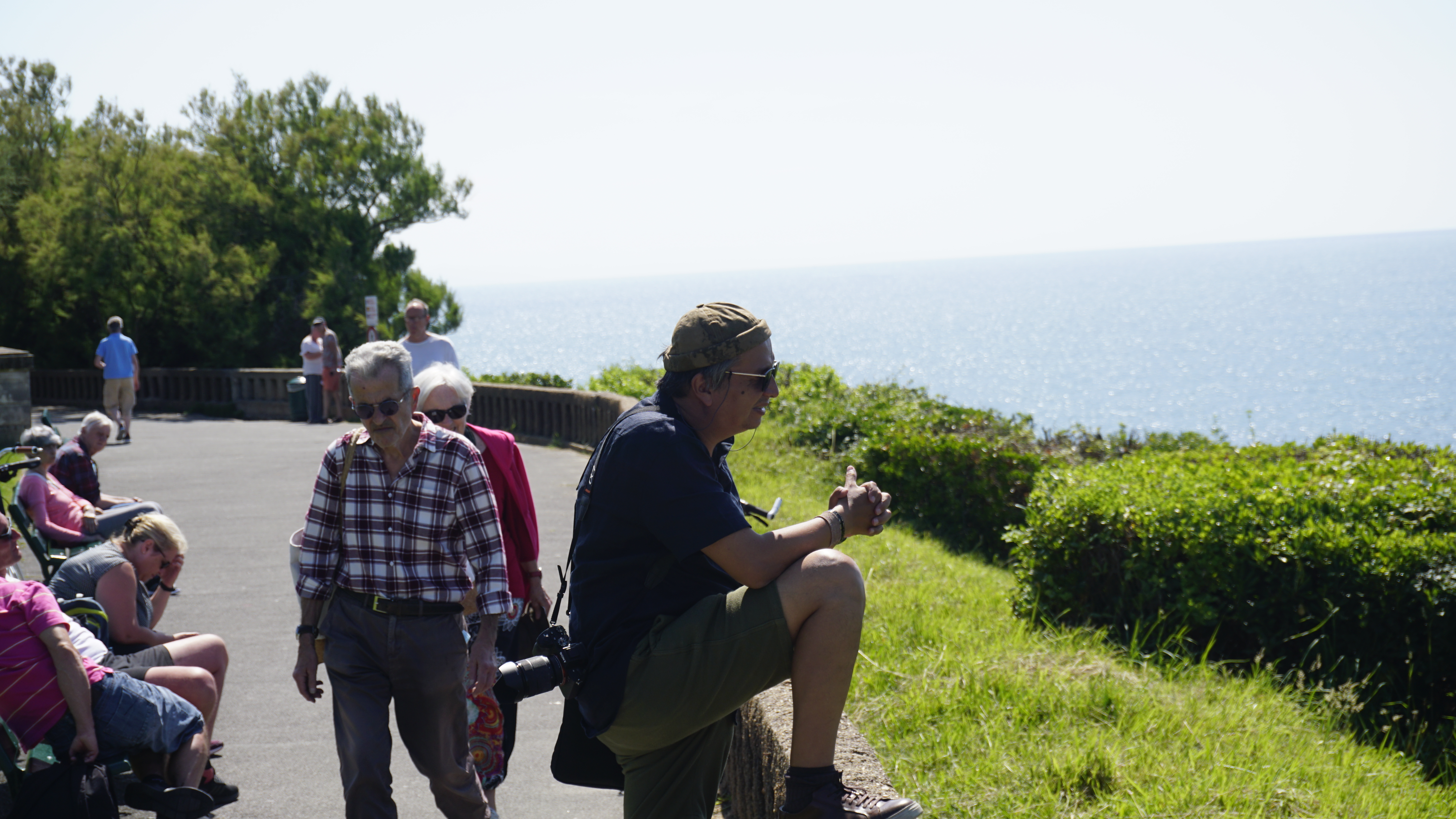 A photographer and other visitors pause beside a seaside promenade.