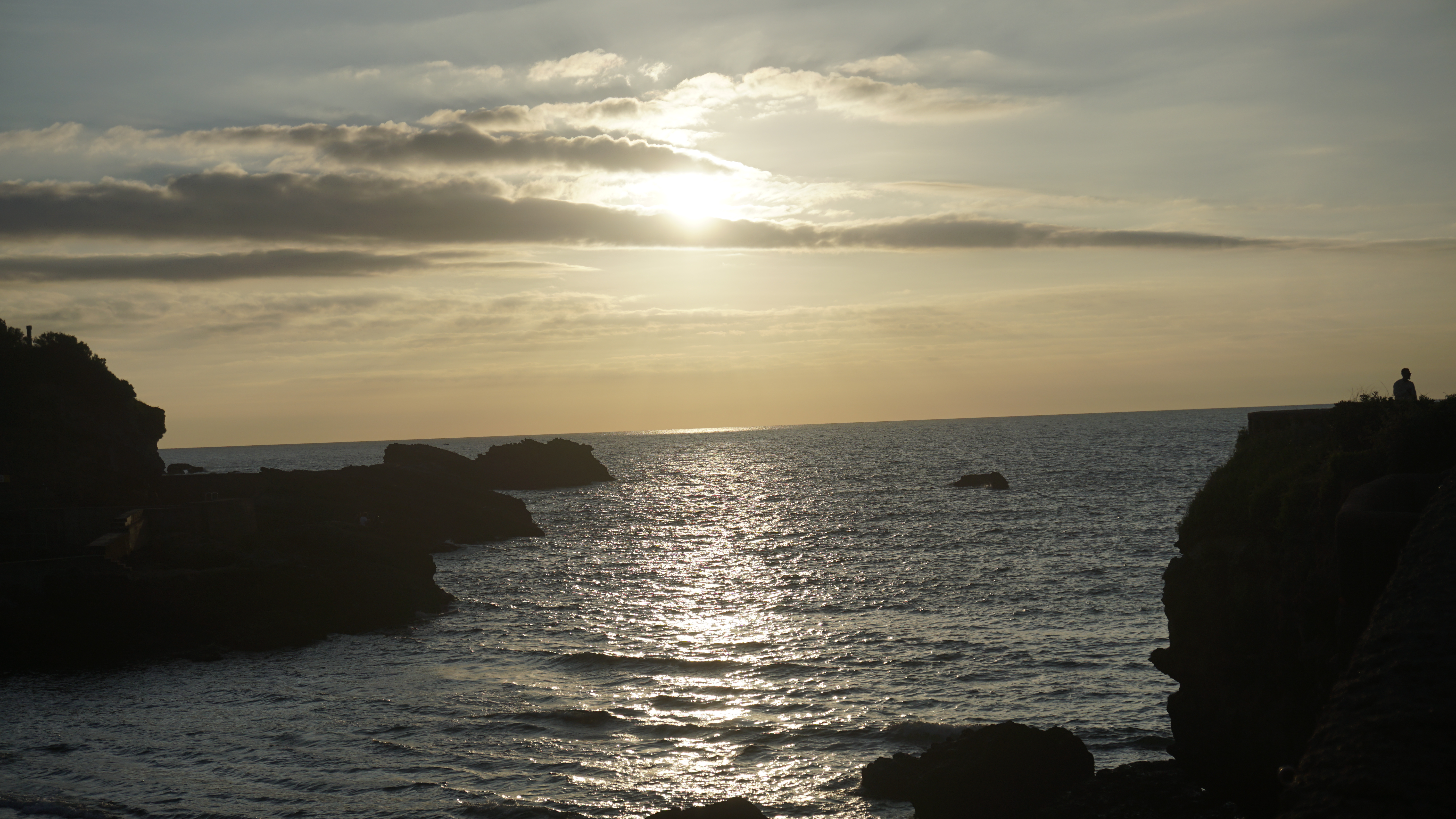 Golden sunlight crosses the sea between dark coastal rocks.