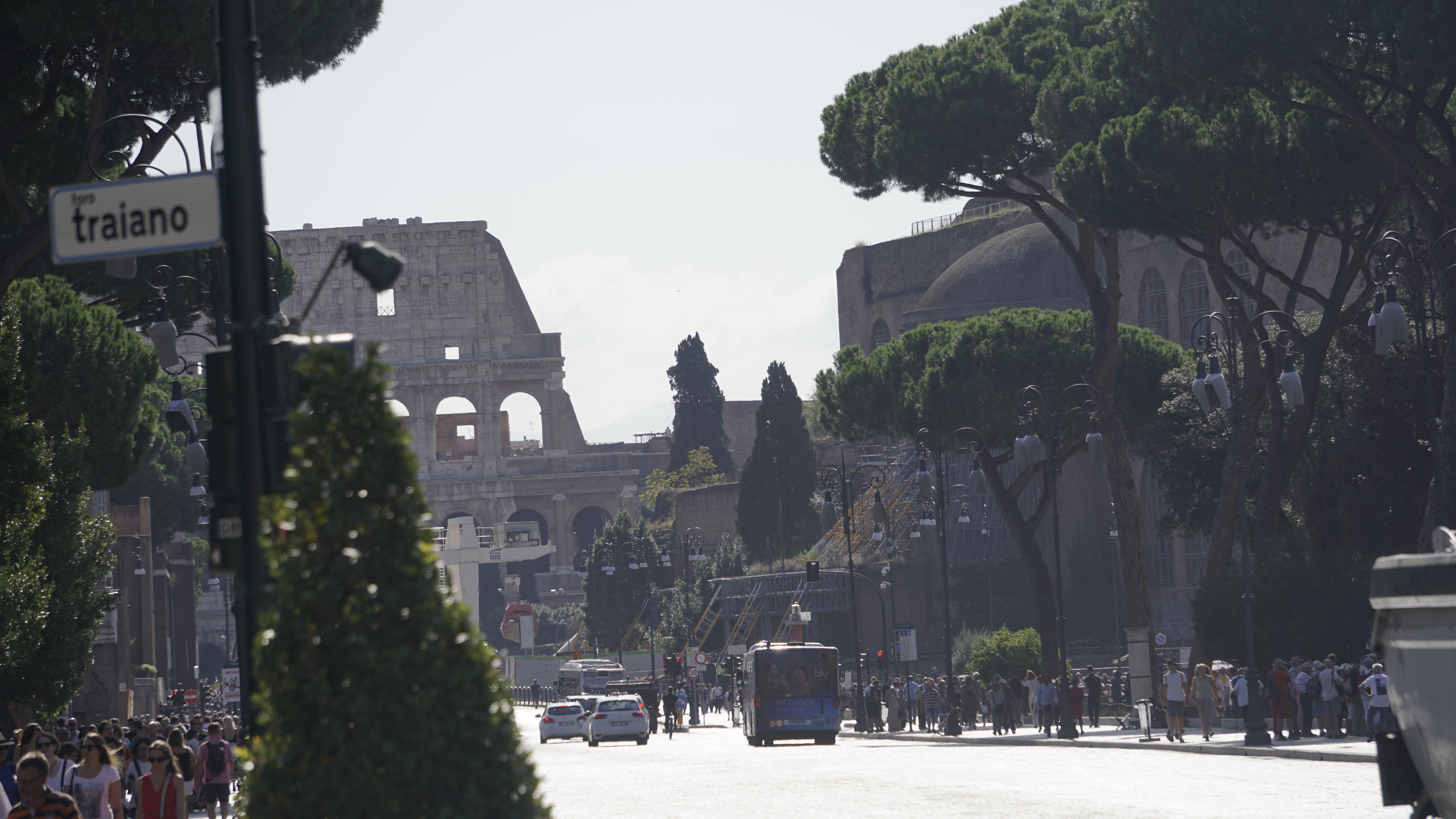 A busy street of walkers and vehicles with the Colosseum beyond.