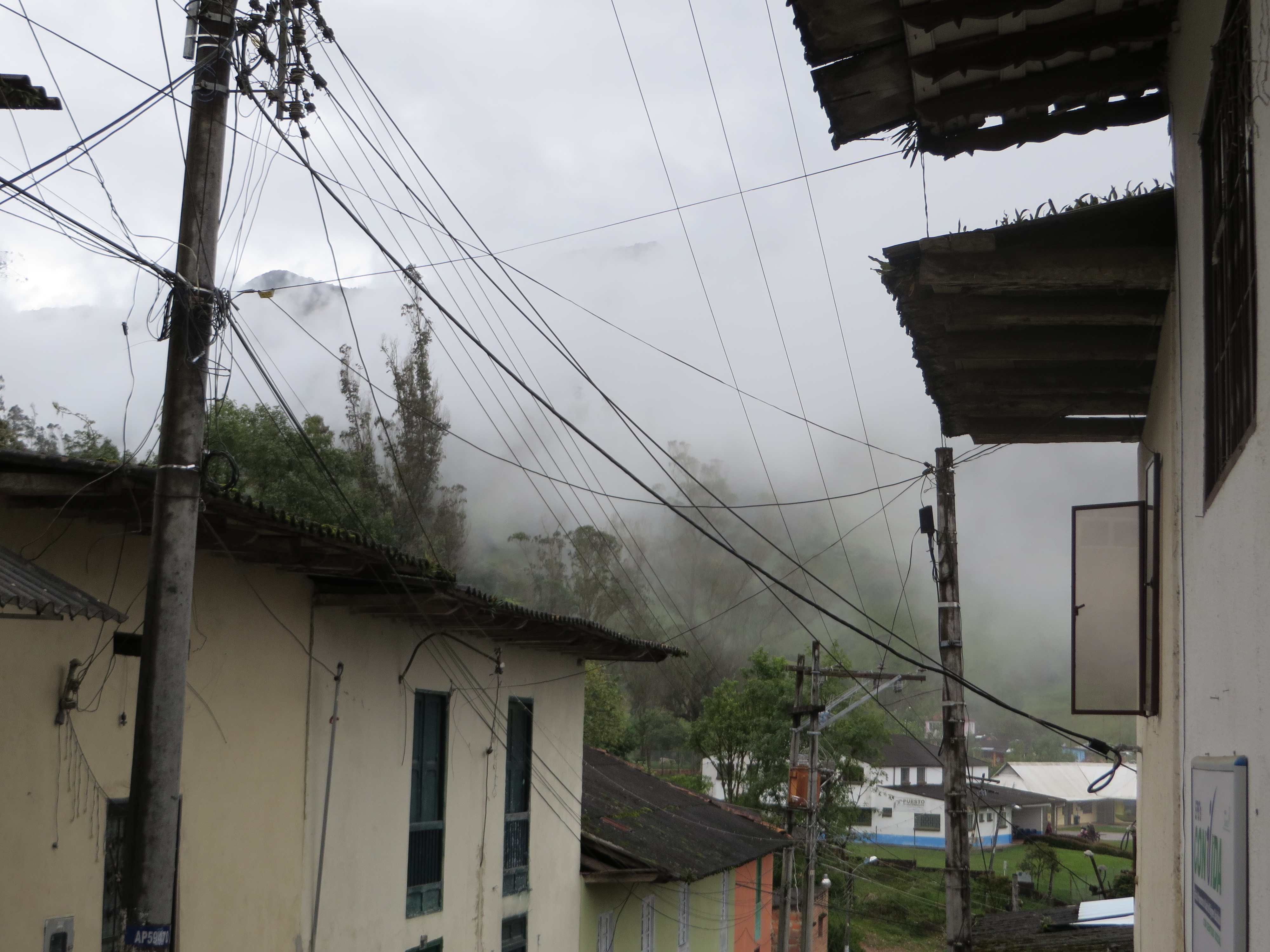 A town and overhead wires beneath a misty mountain landscape.