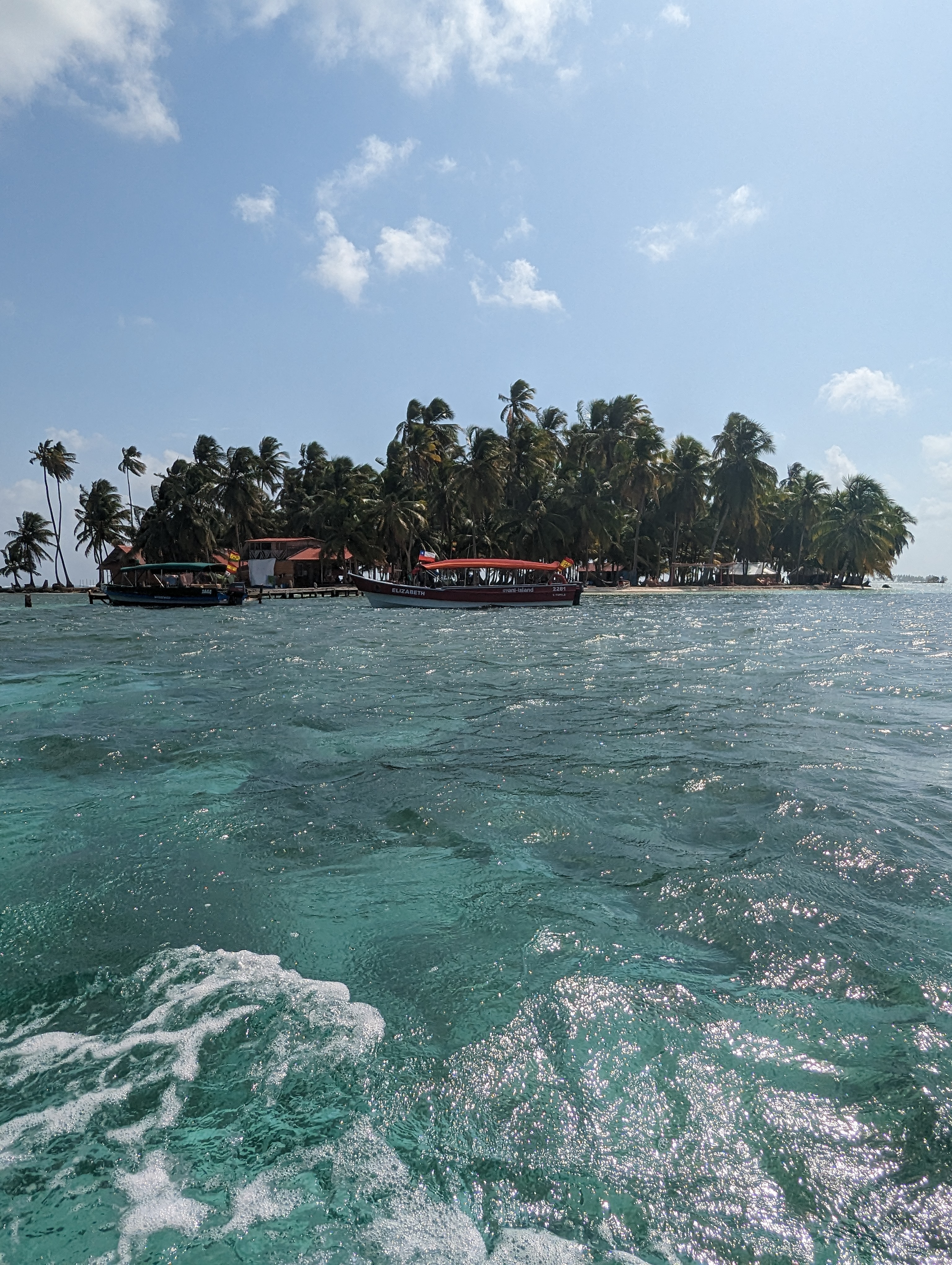Boats float beside a palm-covered island in turquoise water.