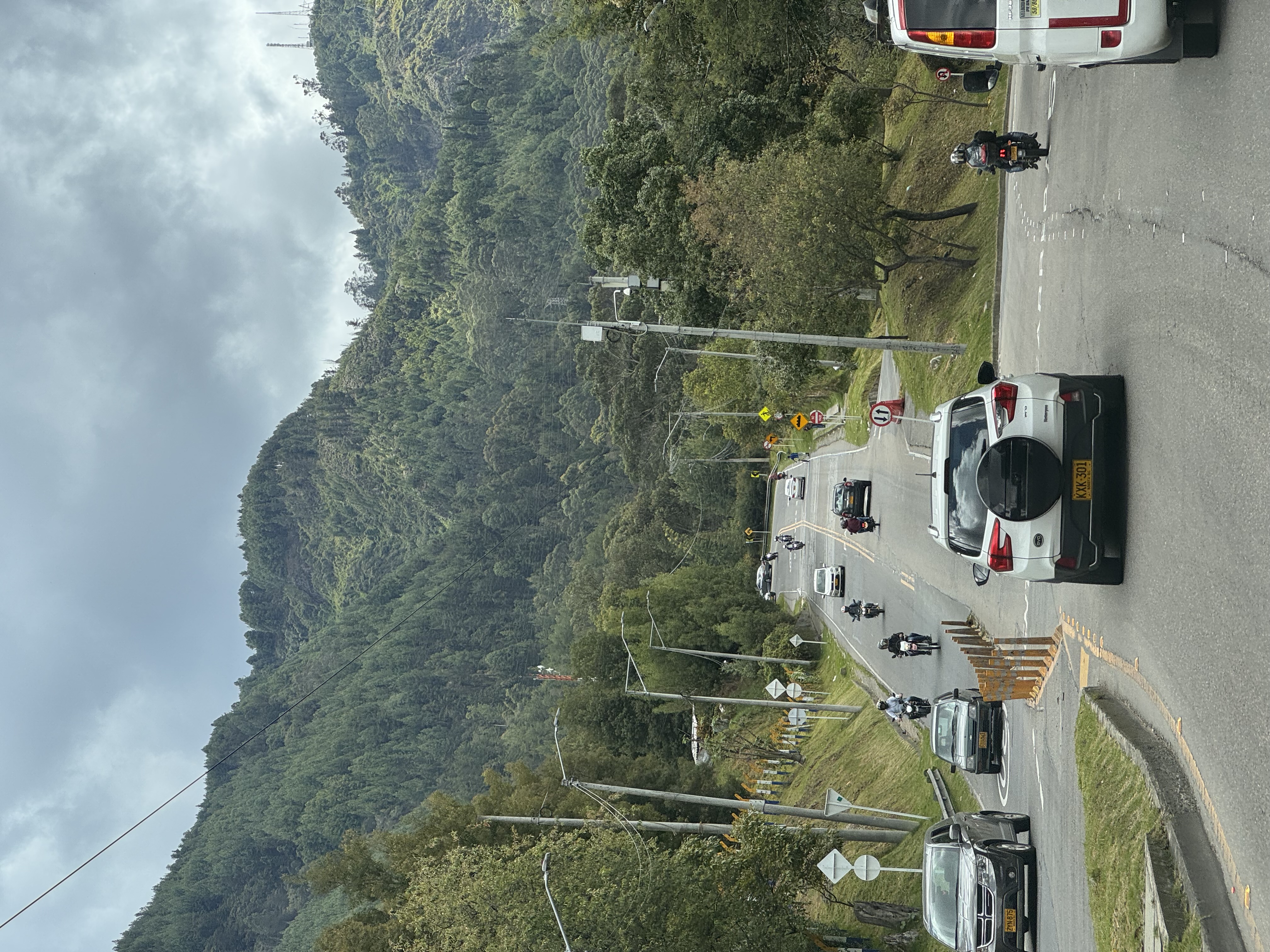 Cars and motorcycles follow a winding road through wooded hills.